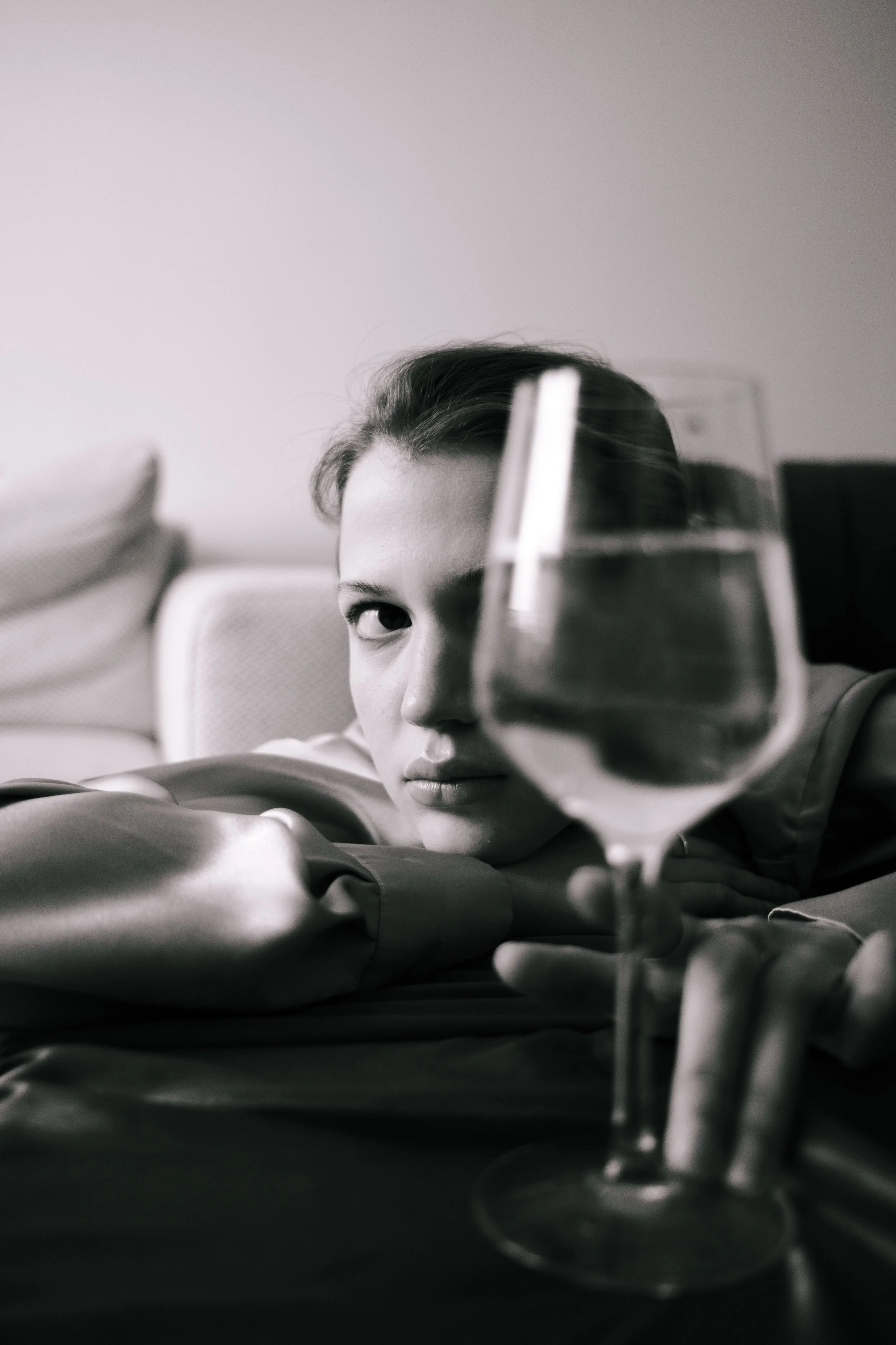 Black and white photo of a woman resting her head on her arm, looking at the camera, with a glass of water in the foreground.