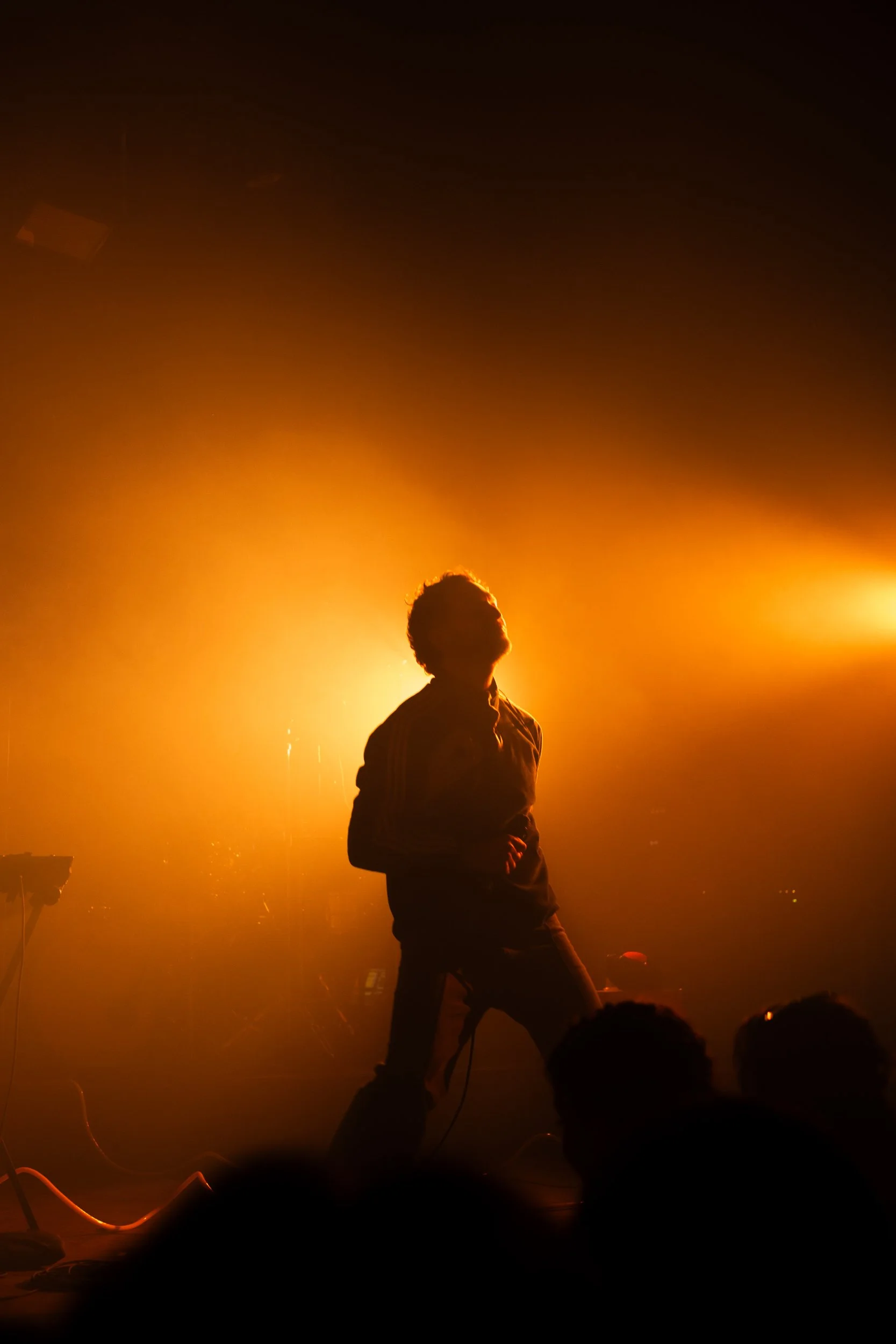 A silhouette of a person standing on a stage illuminated by warm yellow and orange lights, during a live performance or concert.