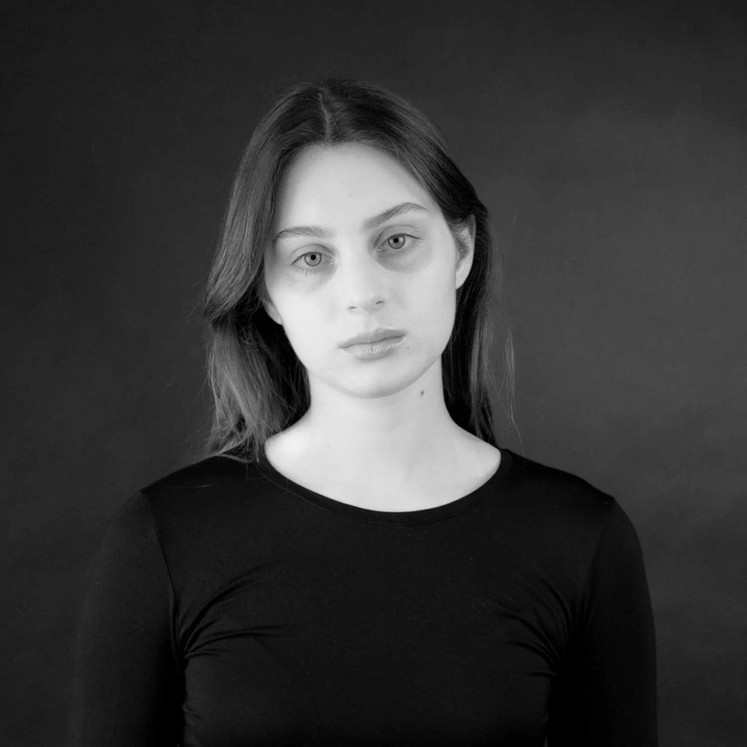 Black and white portrait of a woman with shoulder-length hair, wearing a black top, against a dark background.
