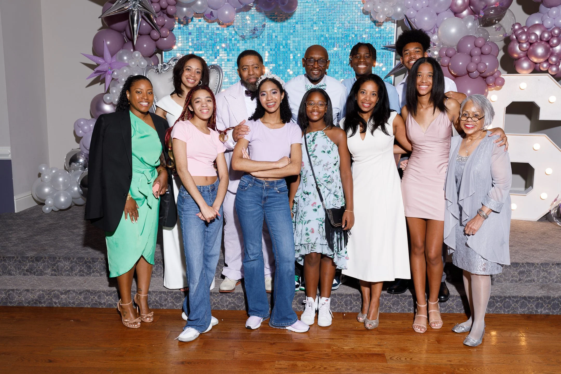 Group of diverse people posing together at a celebration or event with decorative balloons and backdrop.