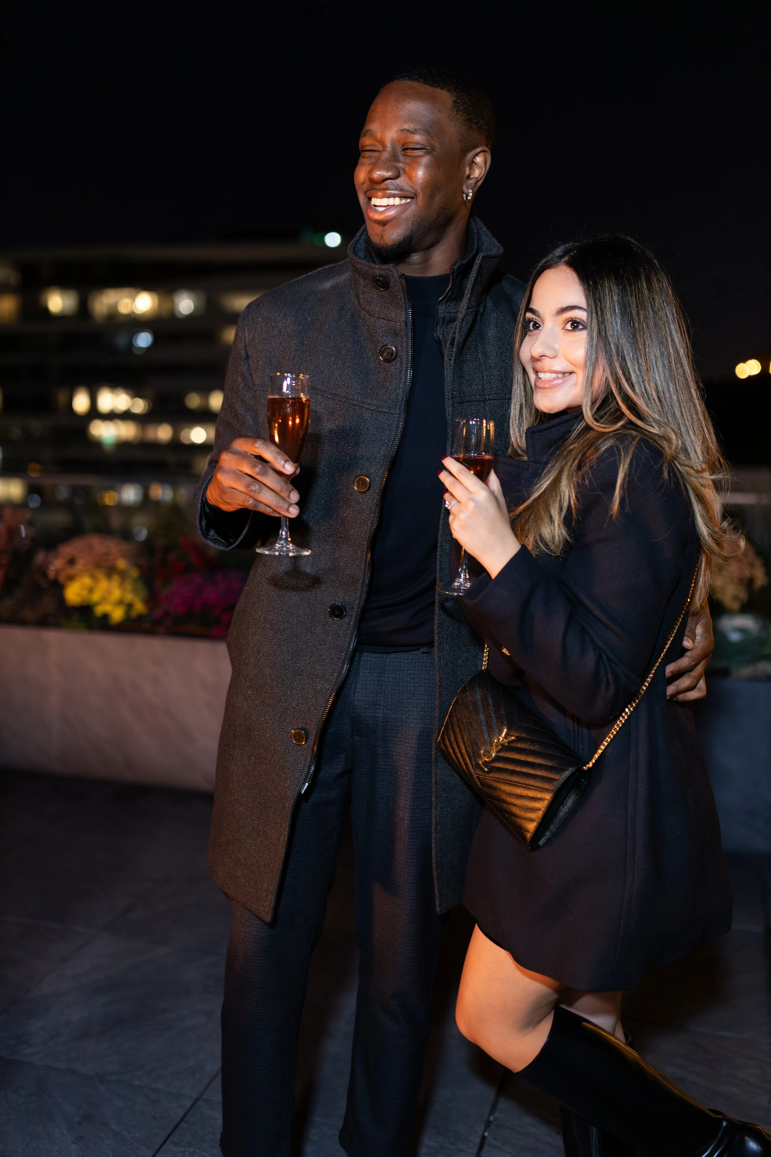 A man and woman holding glasses of rosé wine at a nighttime outdoor event, smiling and enjoying each other's company.