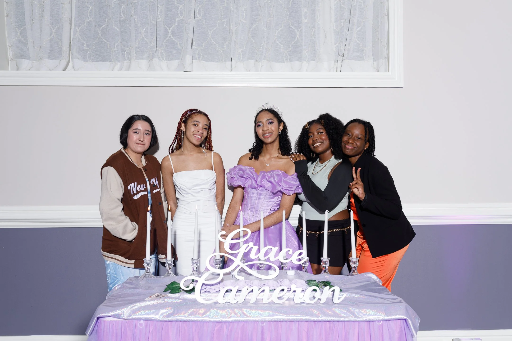 Five young women standing behind a table at a celebration, with a sign that reads 'Grace Cameron,' surrounded by candles and decorative elements.