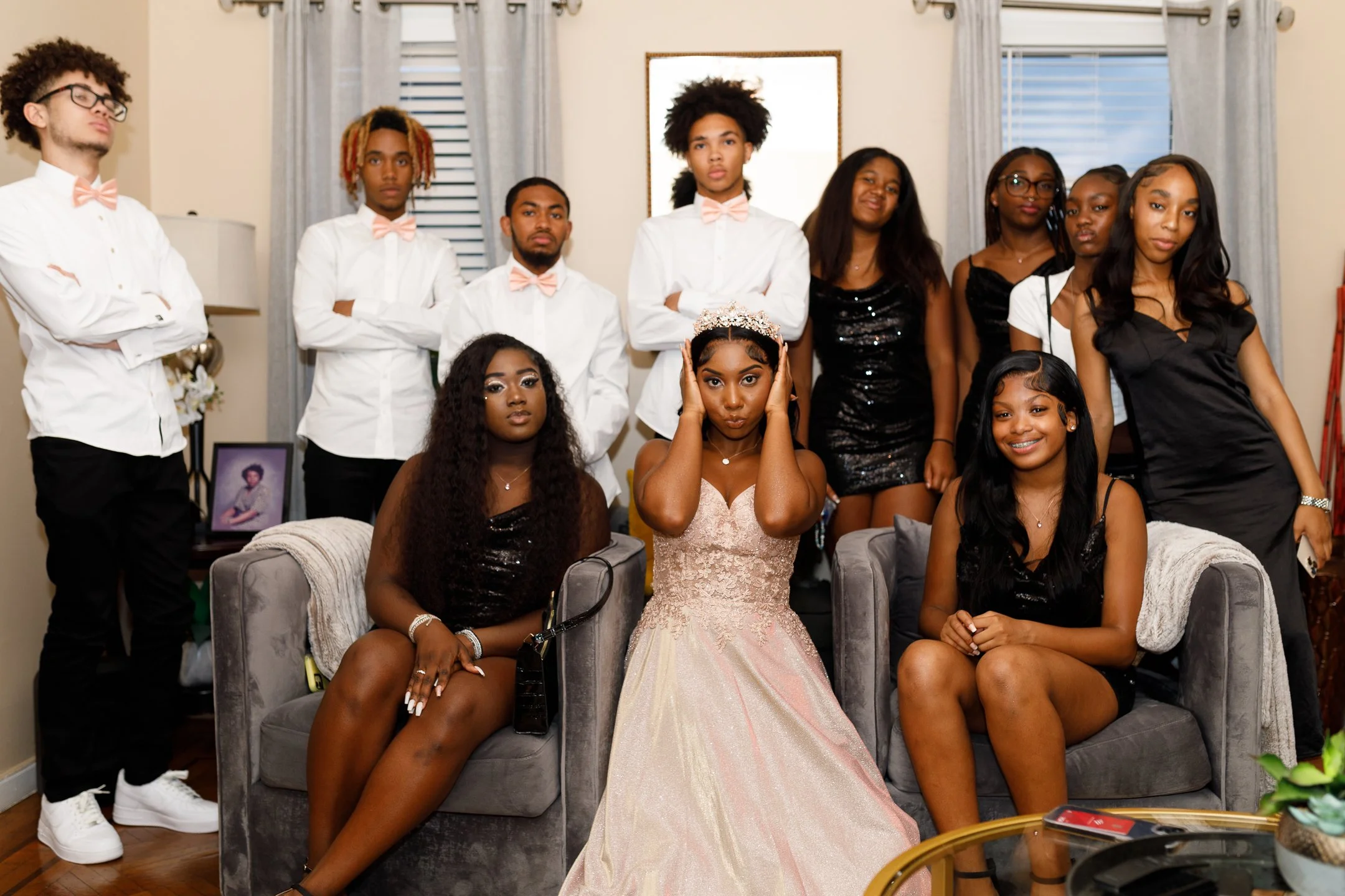 Group of young people at a quinceañera, with the birthday girl in a pink gown and tiara, seated on a gray couch with two friends.