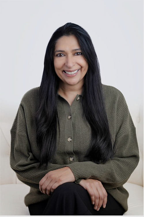 Woman with long black hair smiling, wearing a green button-up sweater, seated against a plain light background.