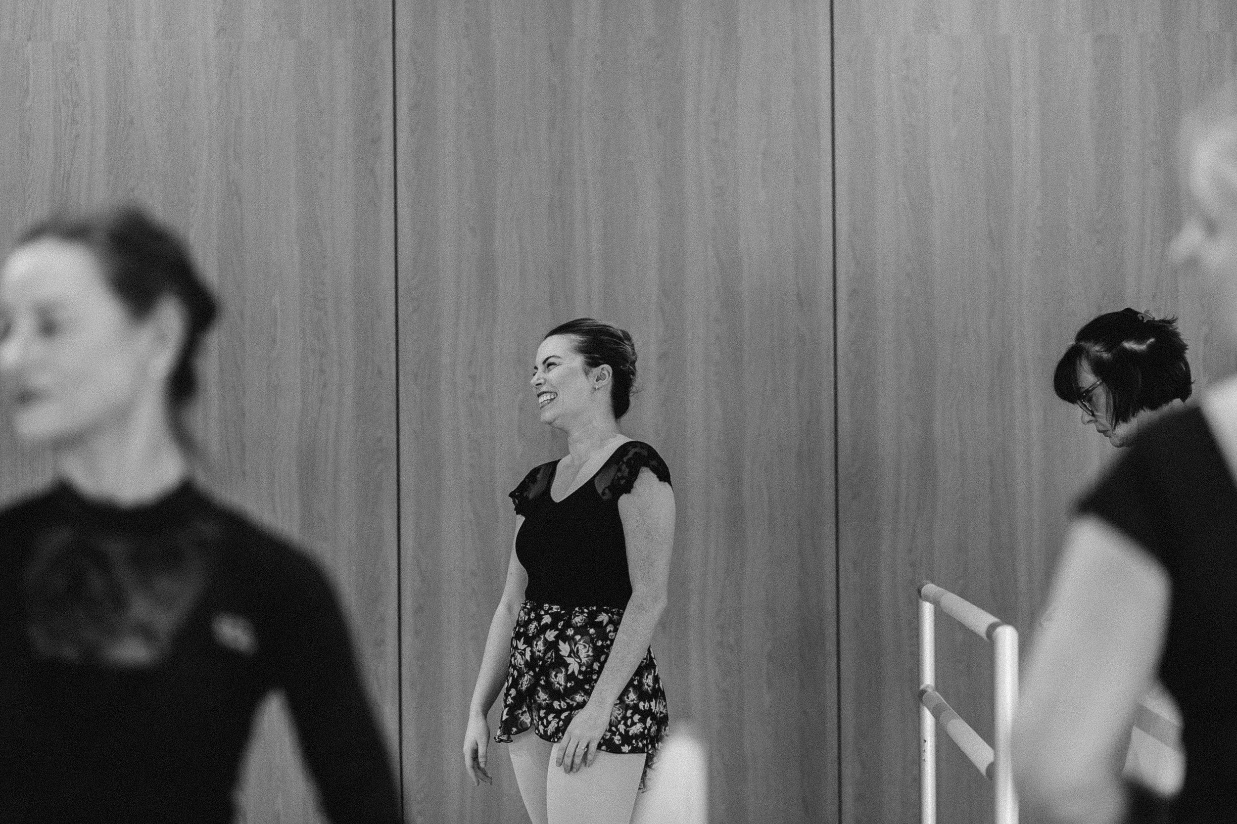Black-and-white photo of a smiling woman in a floral skirt standing in a dance studio.