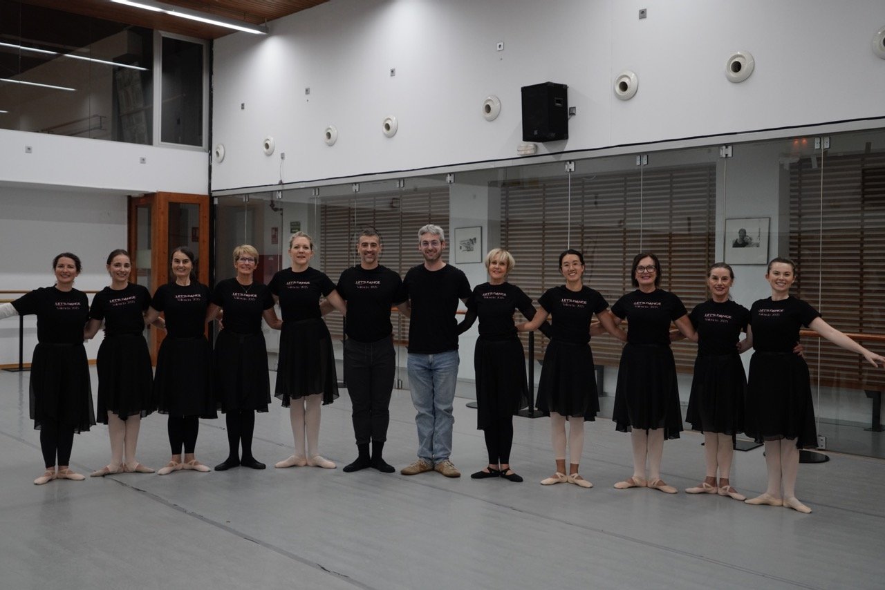 Ballet dancers and instructor posing together in a dance studio.