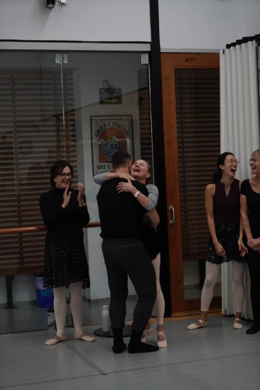 People laughing and embracing during a dance rehearsal in a studio.