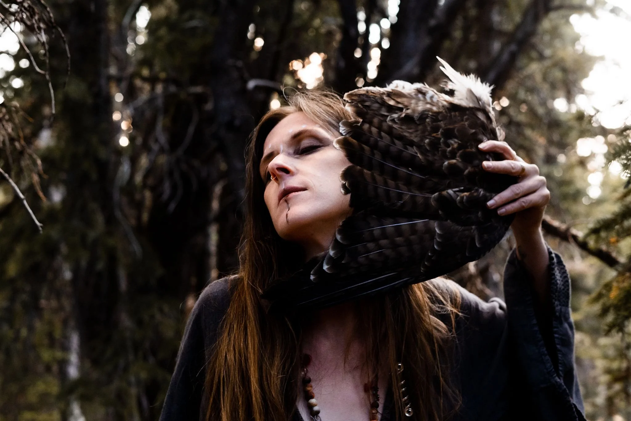 Shamanic woman, Alyssa, waving feathers in front of her face in the woods.