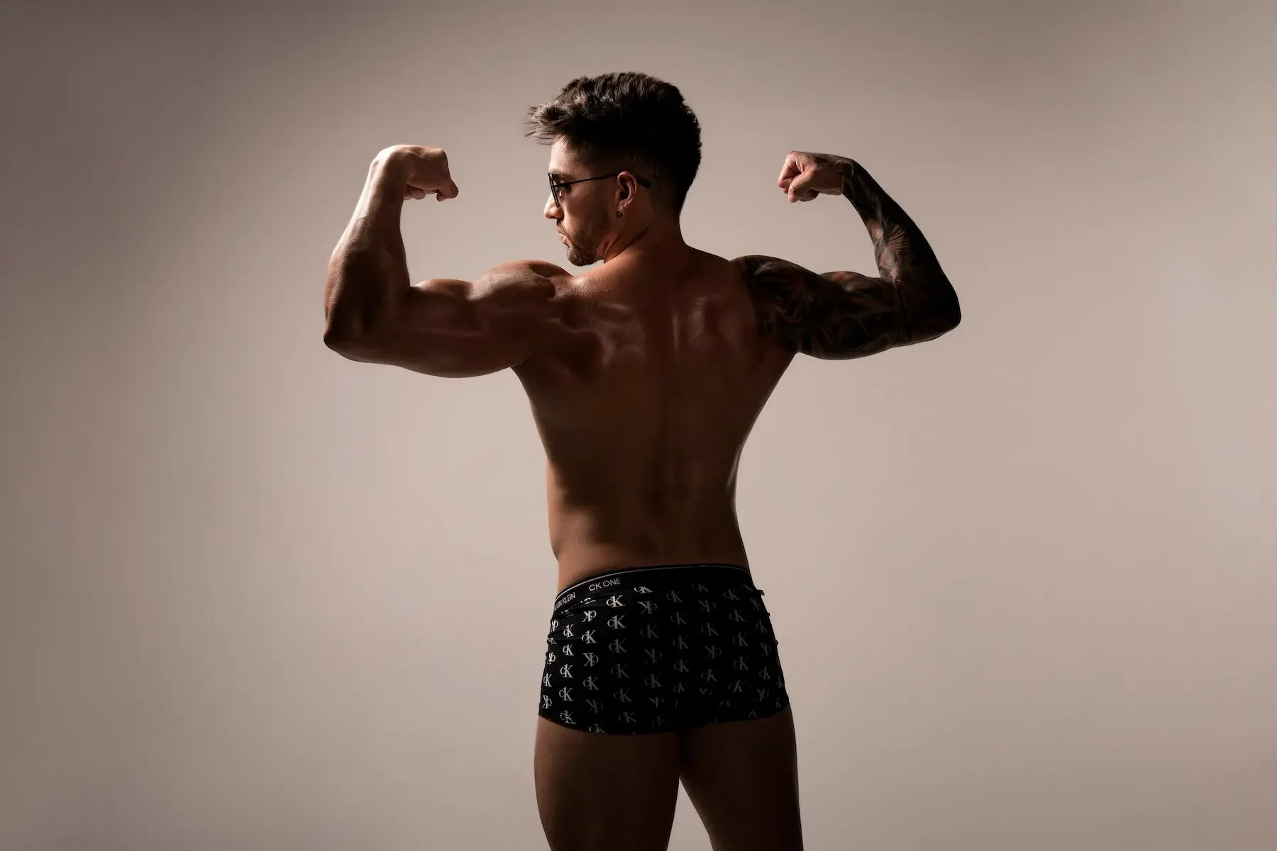 Hombre musculoso en ropa interior, de espaldas, posando con brazos flexionados.