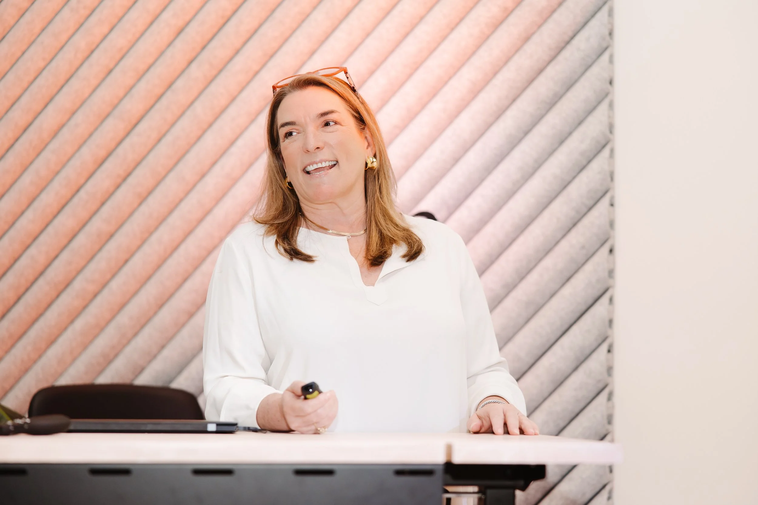 Rebecca Green, real estate business coach giving a presentation at a conference or meeting, holding a remote control in her right hand, with a smiling expression.