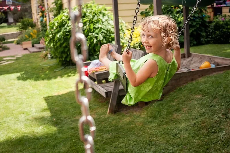 A child with blonde hair swinging outside.