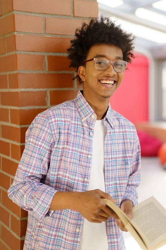 A teen boy smiling in front of a brick wall.