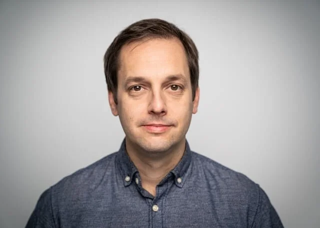 A man with brown hair, wearing a grey shirt