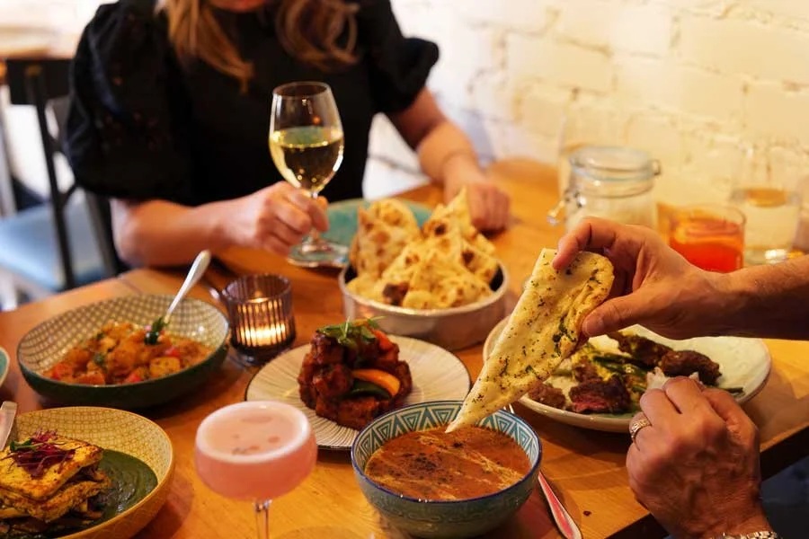A woman holds a glass of white wine over a table full of Indian dishes at Pukka Toronto