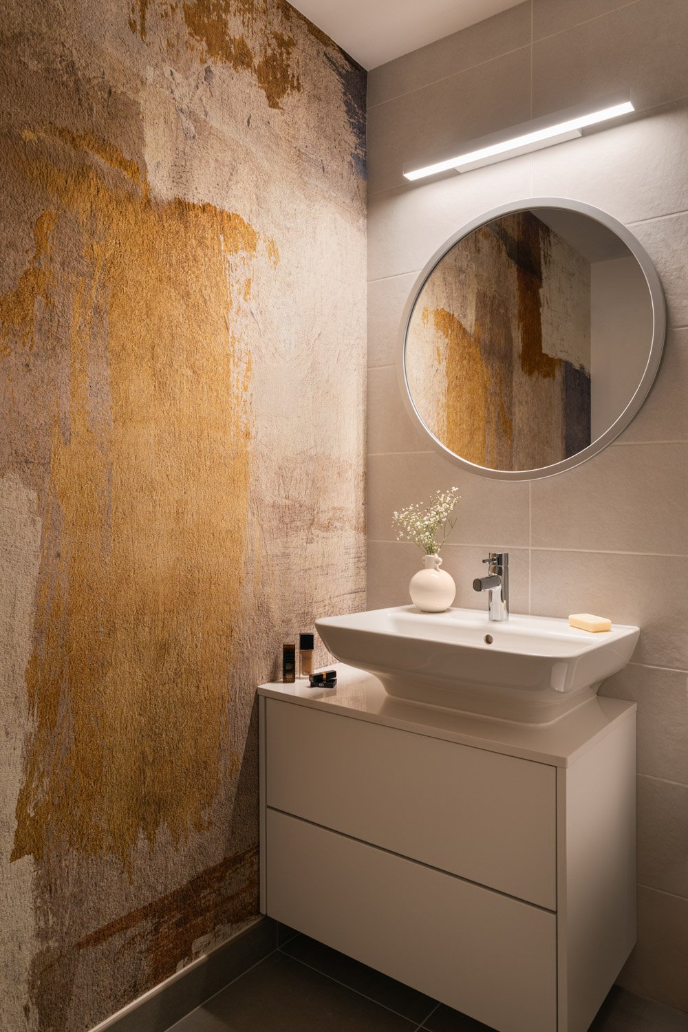 Modern bathroom vanity with a round mirror and textured gold accent wall.