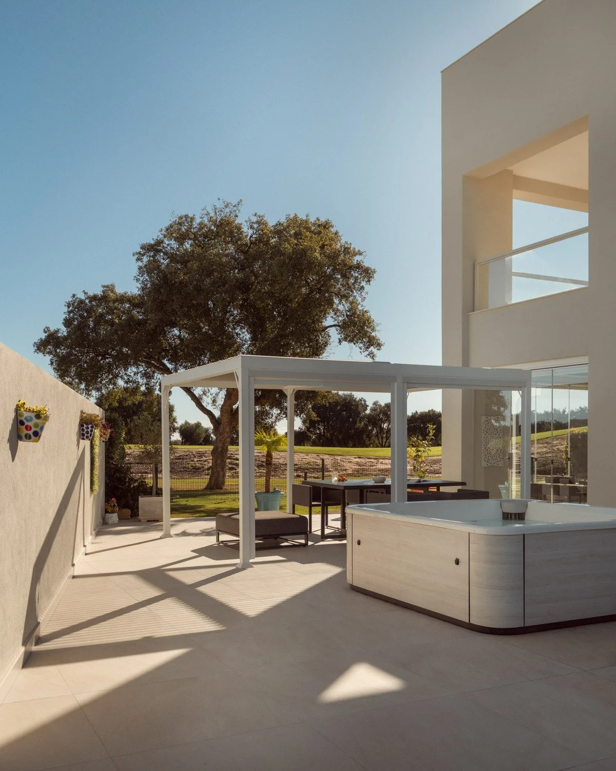 Modern white villa terrace featuring a hot tub and dining pergola.