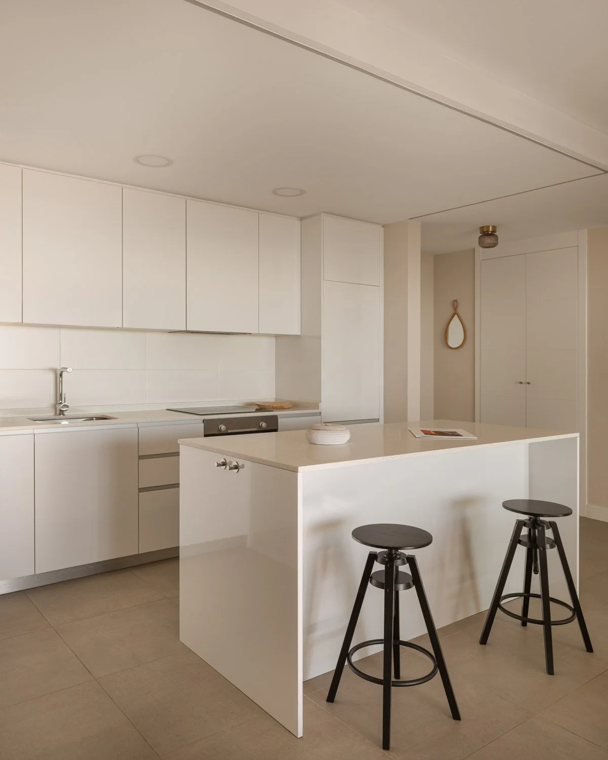 Modern white minimalist kitchen with an island and black bar stools.