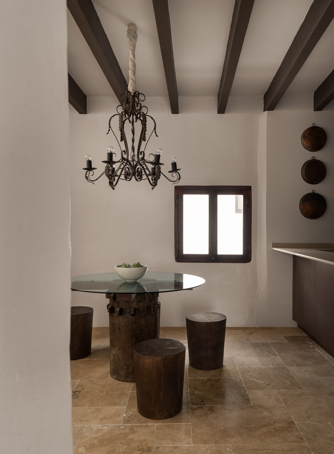 Dining nook with antique wrought iron chandelier and wooden stump stools in Altea townhouse