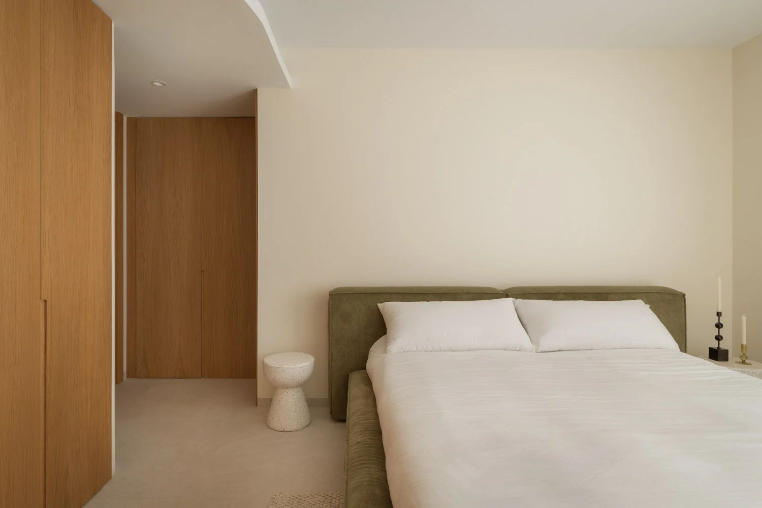 Minimalist bedroom with a green headboard and custom oak wardrobe.