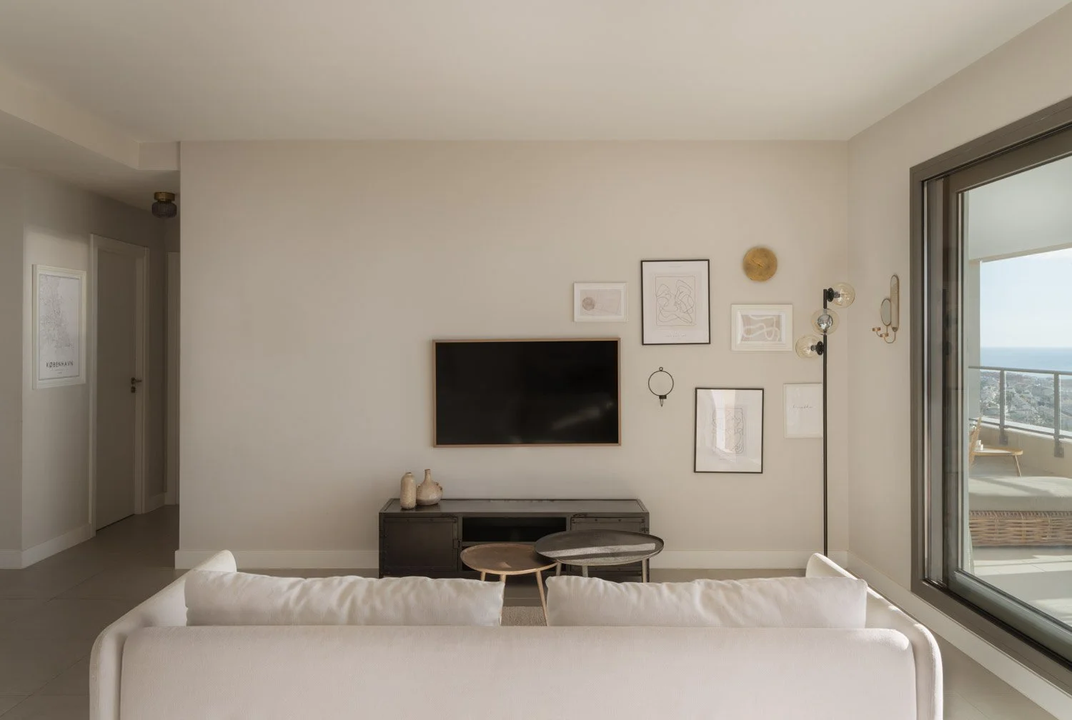 Modern stylized living room with framed art, TV, and balcony overlooking the sea.