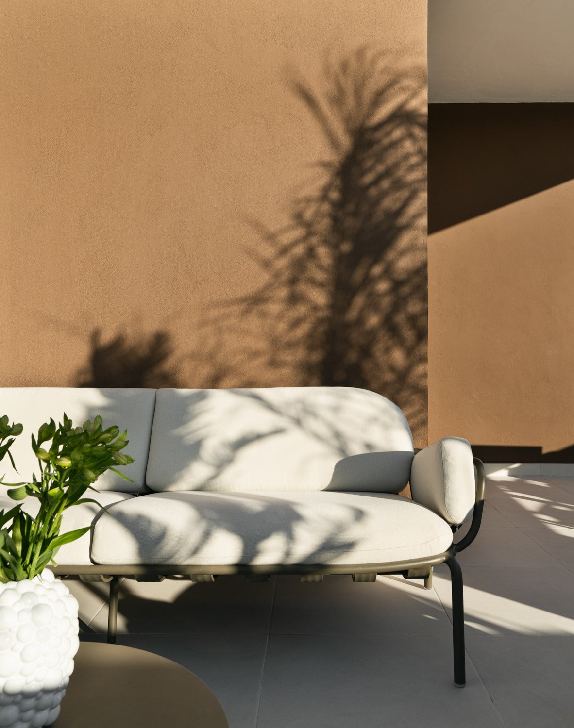 Outdoor terrace with a beige lounge sofa and palm tree shadows.
