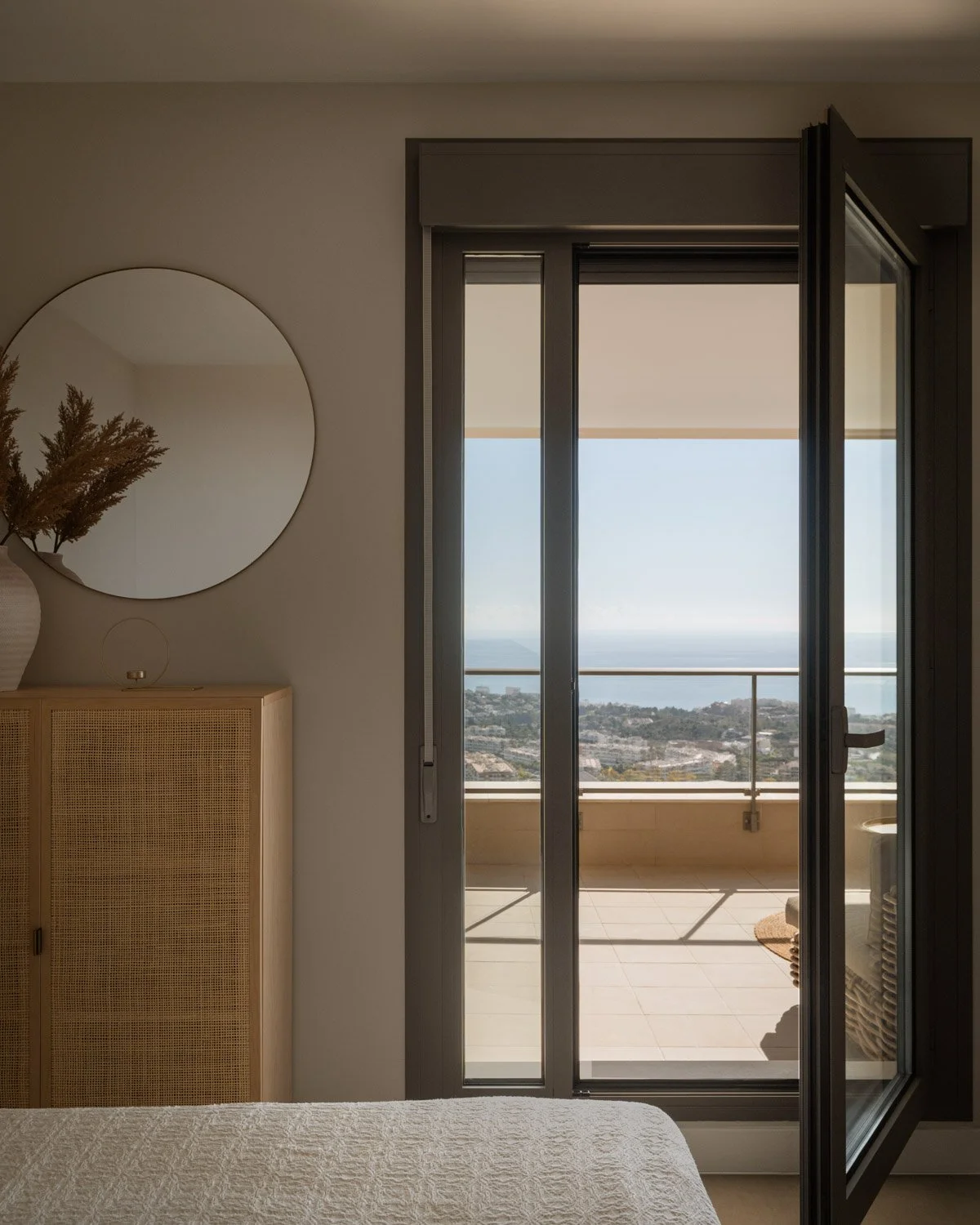 Bedroom with a rattan cabinet and open doors to a sea-view balcony.