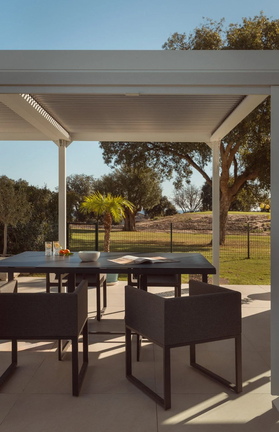Outdoor dining area under a white pergola with a garden view.