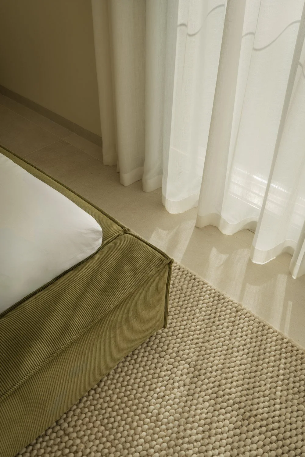 Close-up of a green corduroy bed base and textured rug.