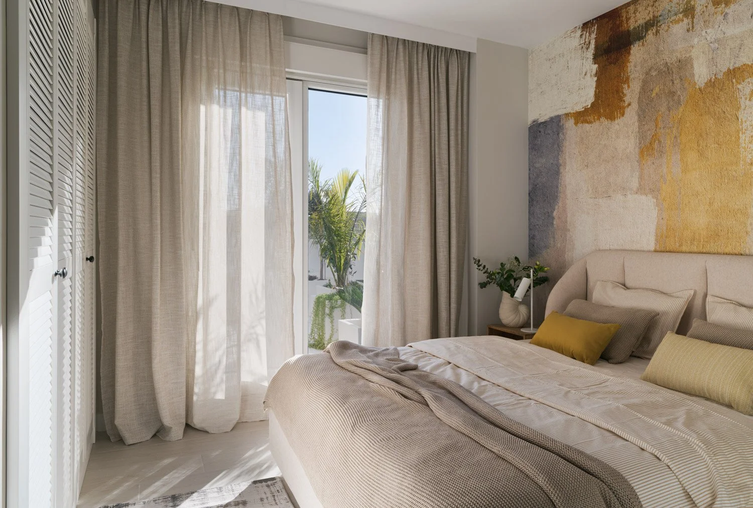 Bright bedroom with a textured wall mural, louvered doors, and balcony access.