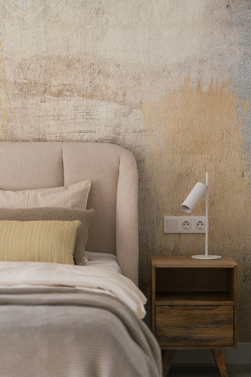 Cozy bedroom styling featuring a textured wall, beige headboard, and wood nightstand.