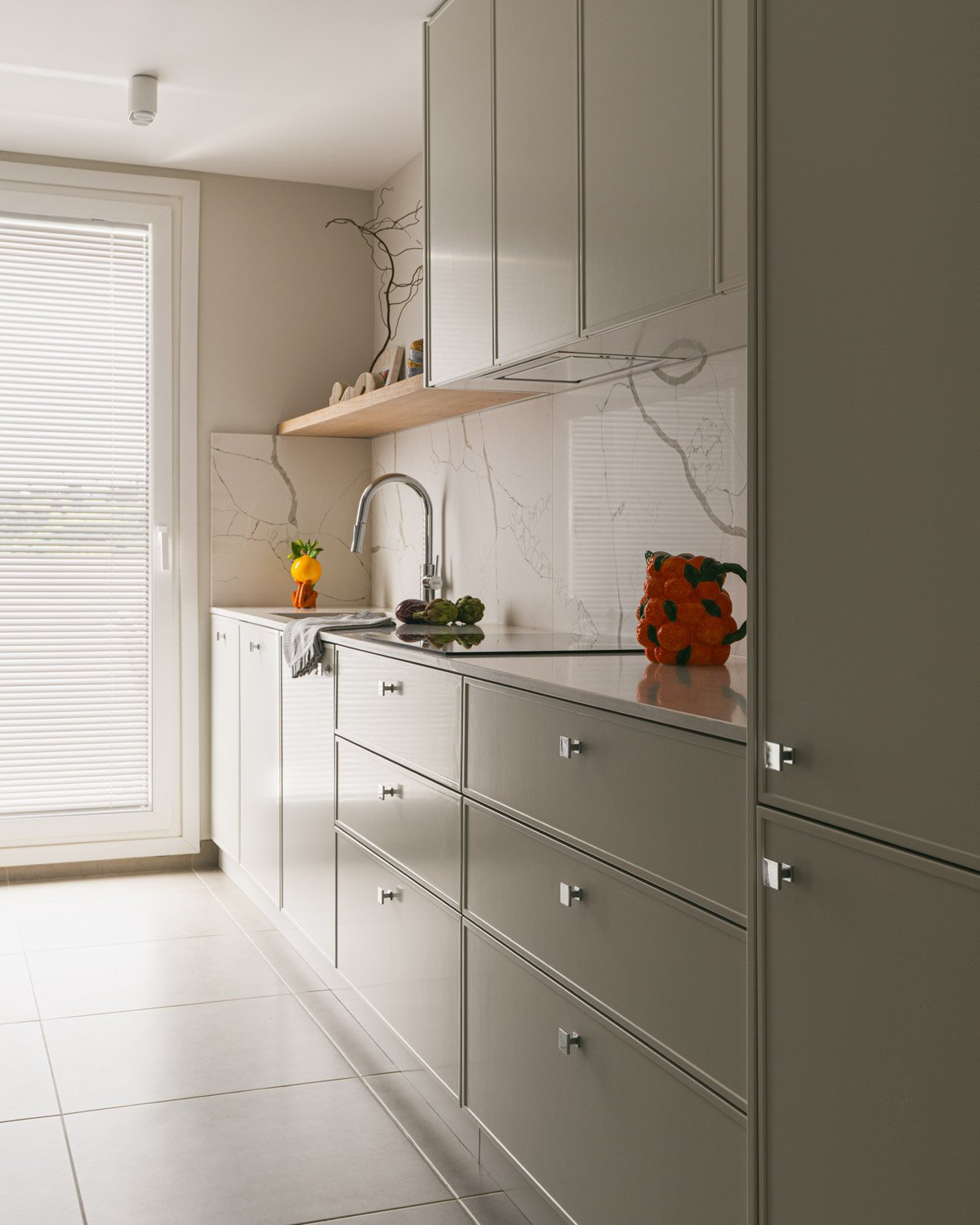 Bright modern kitchen with beige cabinets, marble backsplash, and natural light.