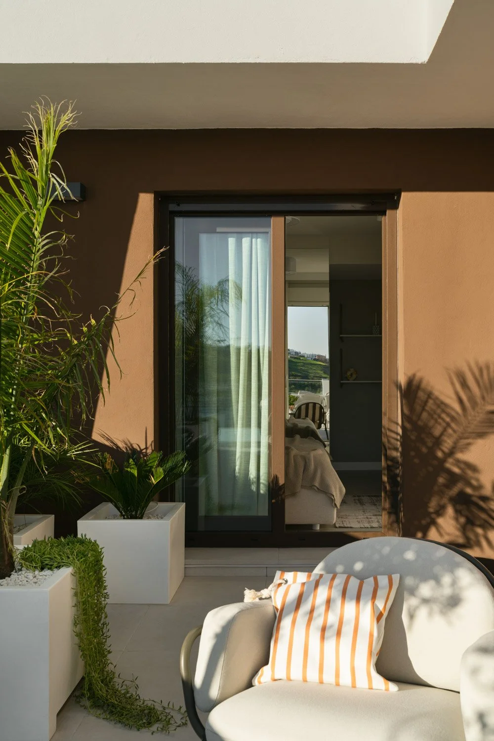 Sunny outdoor terrace with potted plants leading into a bright bedroom.