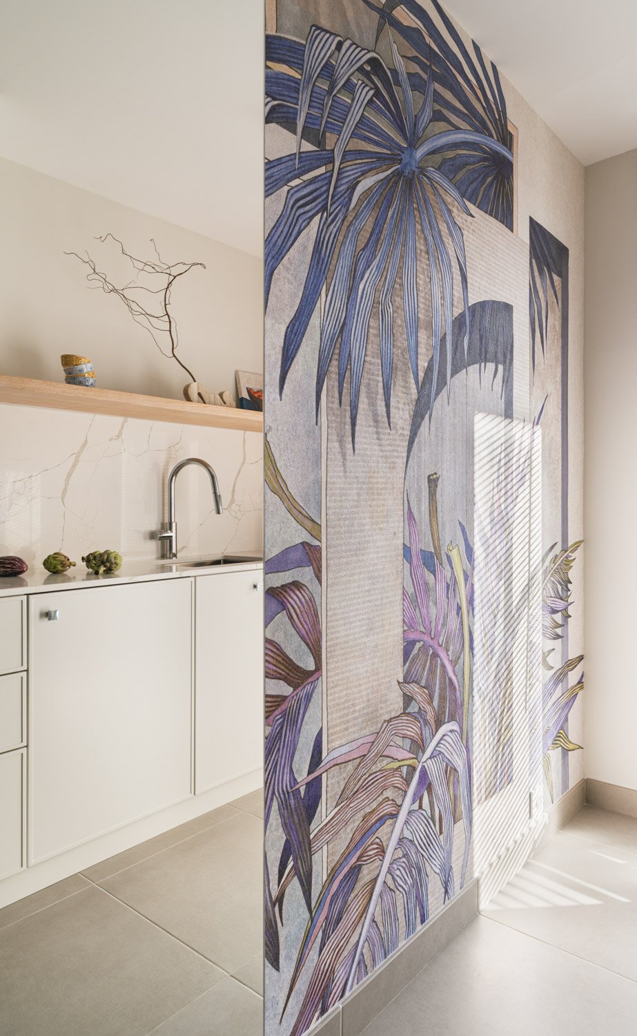 Minimalist white kitchen separated by a wall with tropical botanical mural.