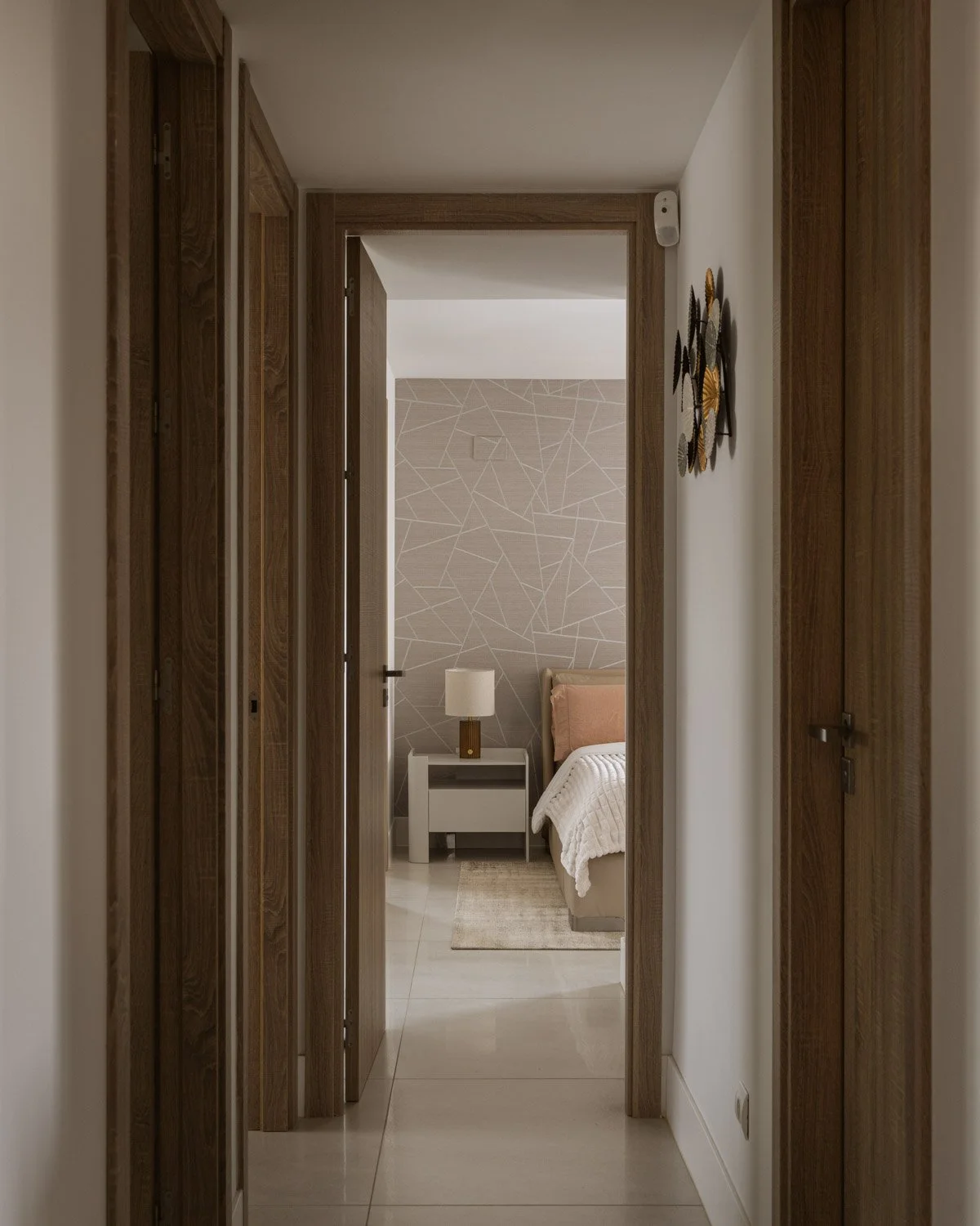 Hallway with wooden doors framing a bedroom with geometric wallpaper.