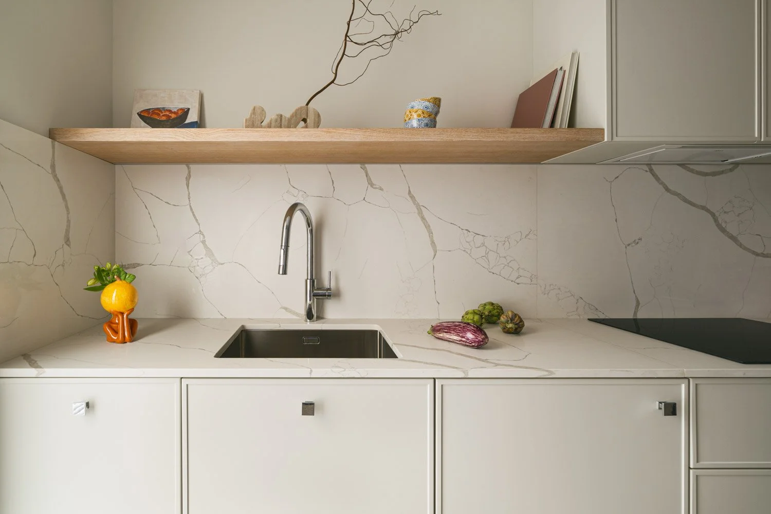 Minimalist kitchen sink detail with marble backsplash and a floating wood shelf.
