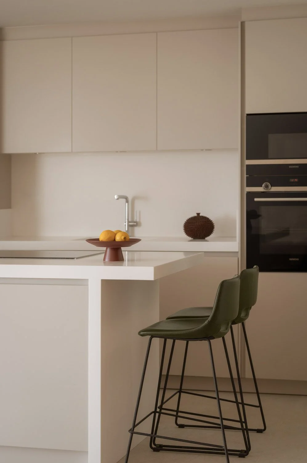 Minimalist white kitchen island featuring dark green leather bar stools.
