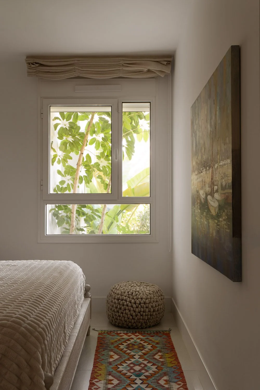 Cozy bedroom corner with a pouf and a window framing greenery.