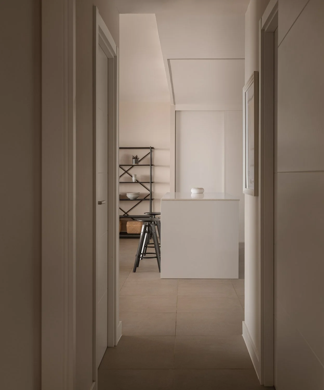 Hallway view framing a modern white kitchen island and black stools.
