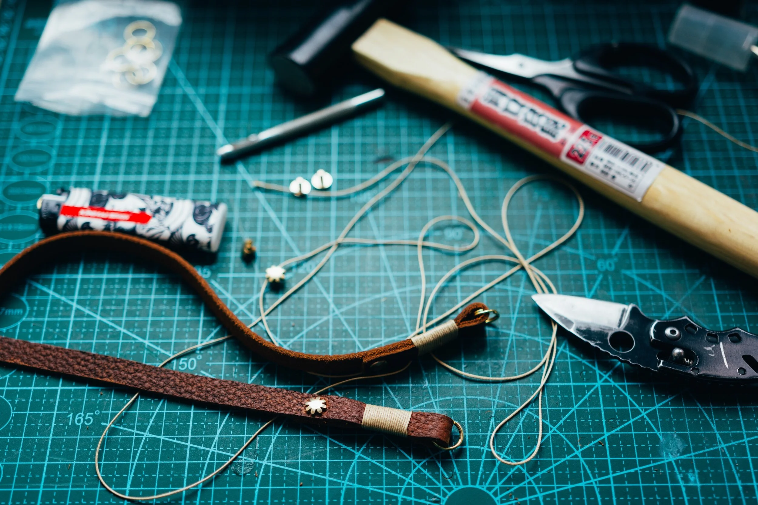 Arbeitsfläche mit Schneidematte, Lederarmbändern, Seil, Messer, Schere, Feuerzeug und Werkzeugen.