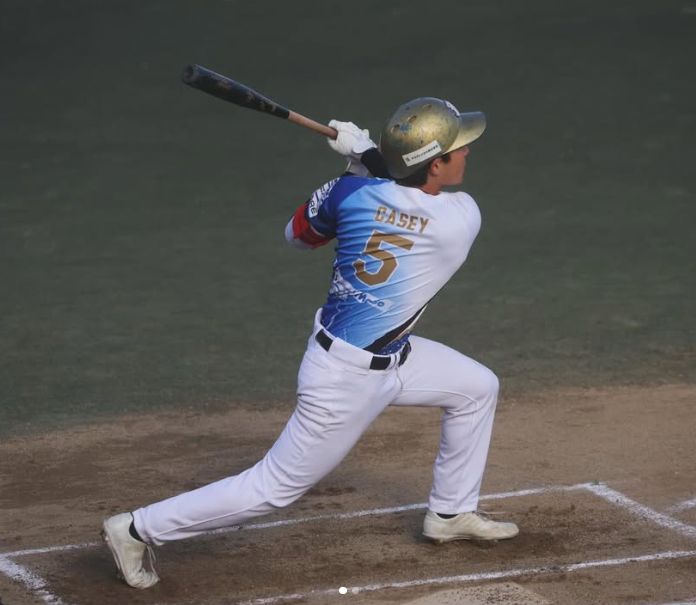A baseball player swings at a pitch from a batting stance on a baseball field.