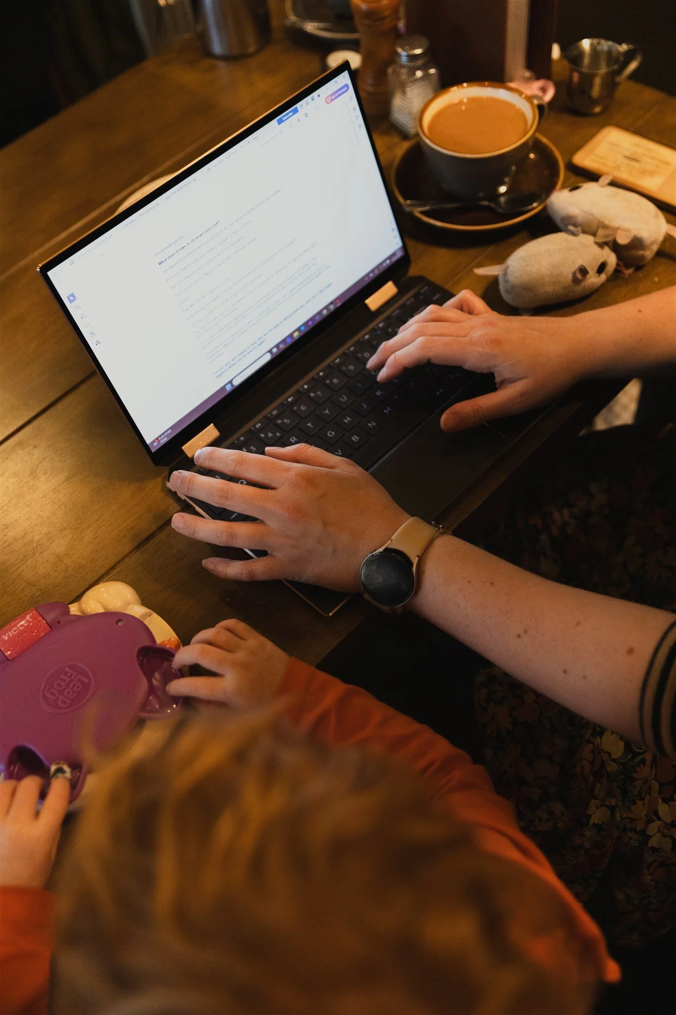 A woman's hands typing at a laptop as a small child types on a toy laptop beside her