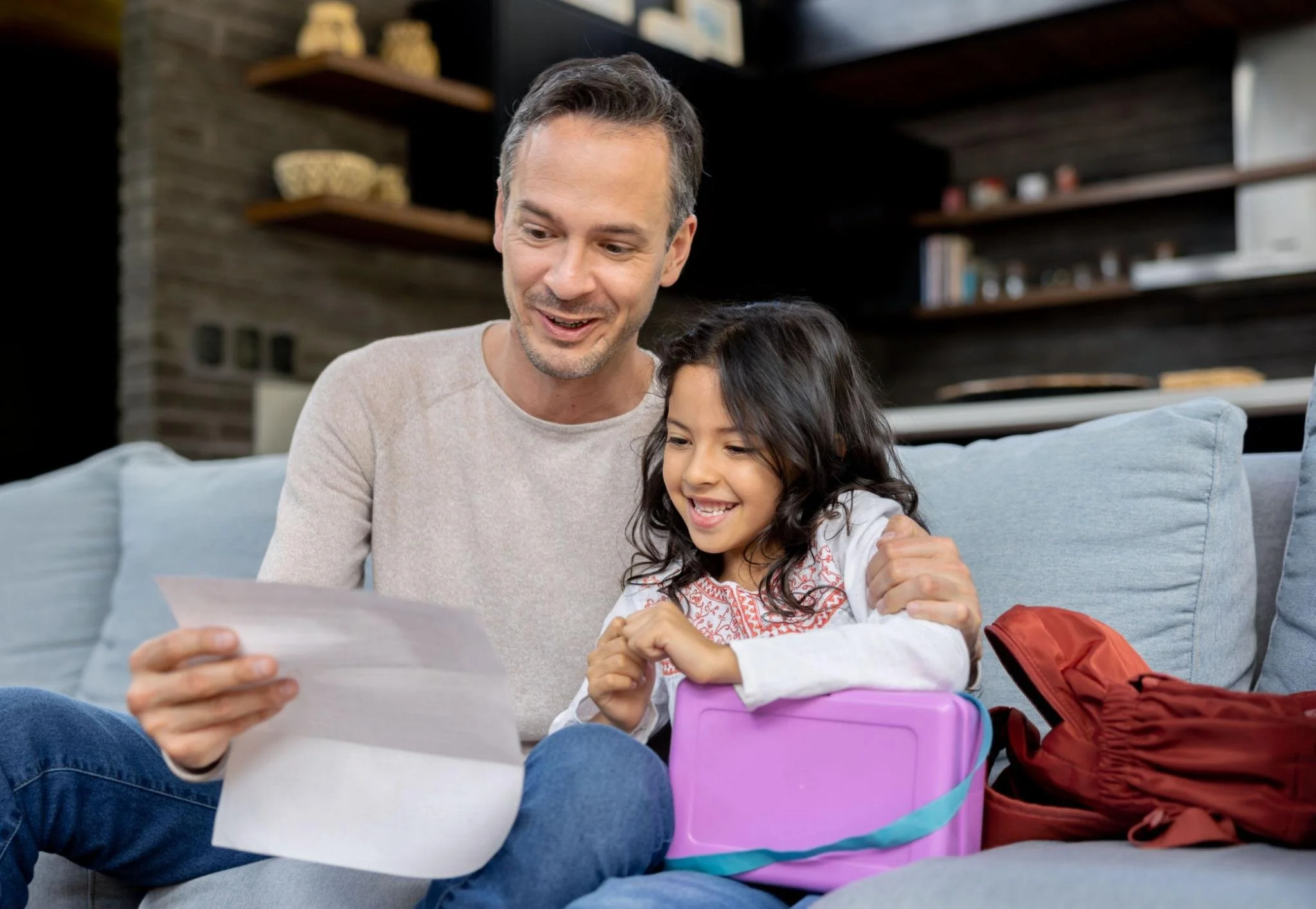 Father and daughter smiling as they review her educational evaluation report at home.