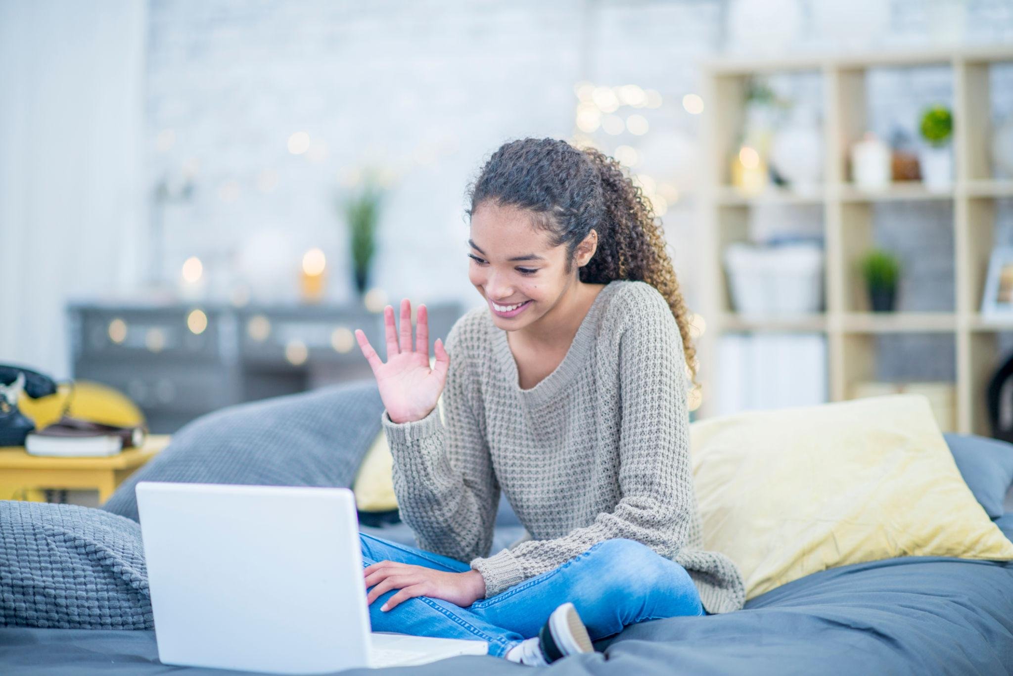 Teenage girl attending an online therapy session on her laptop from a comfortable bedroom.
