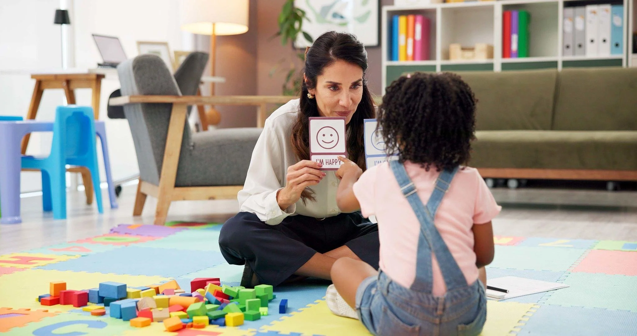Therapist helping a young child identify feelings with emotion cards, illustrating a parent guide to CBT vs. ACT.