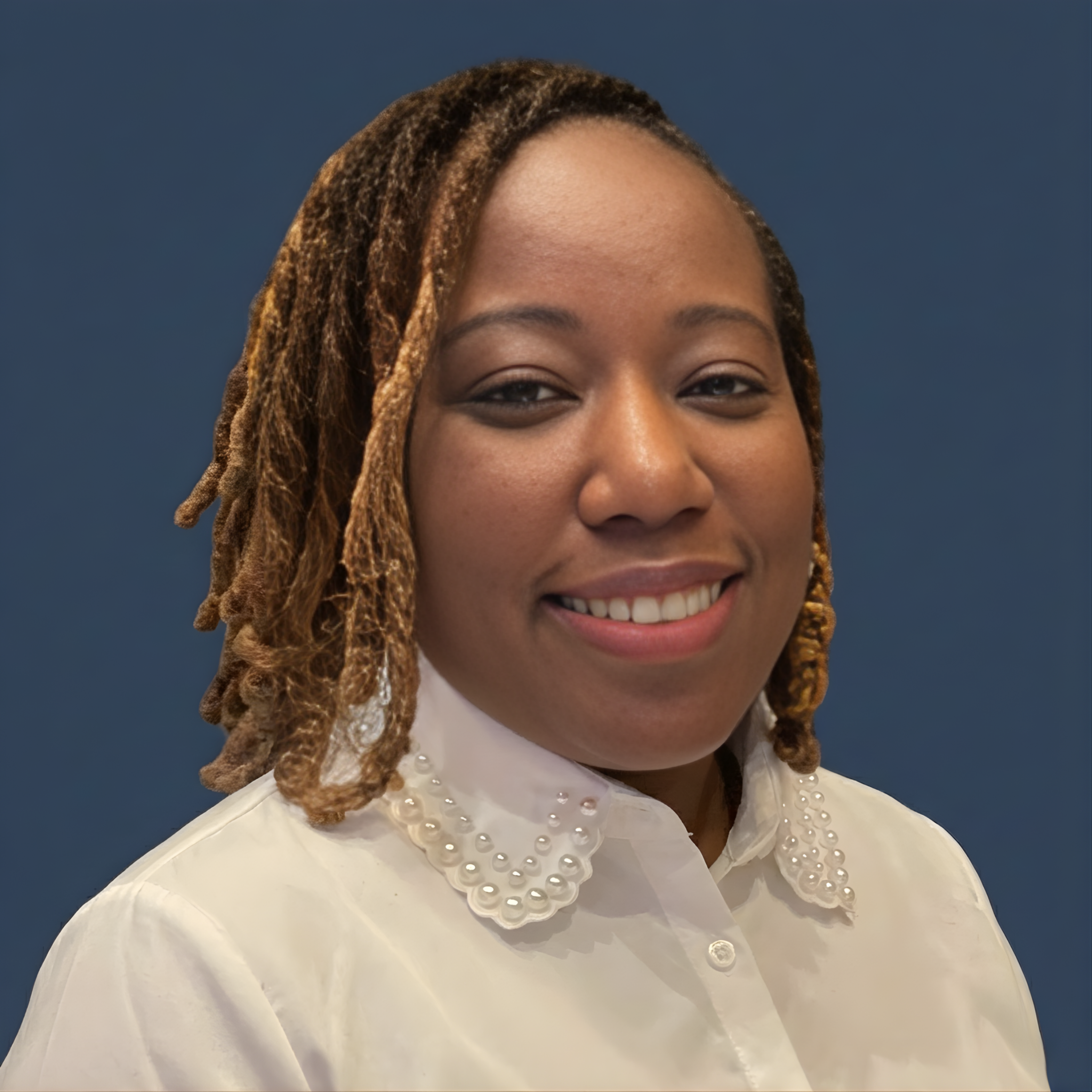 A woman with medium brown skin, styled with shoulder-length dreadlocks, smiling and wearing a white blouse with pearl accents on the collar, against a dark blue background.