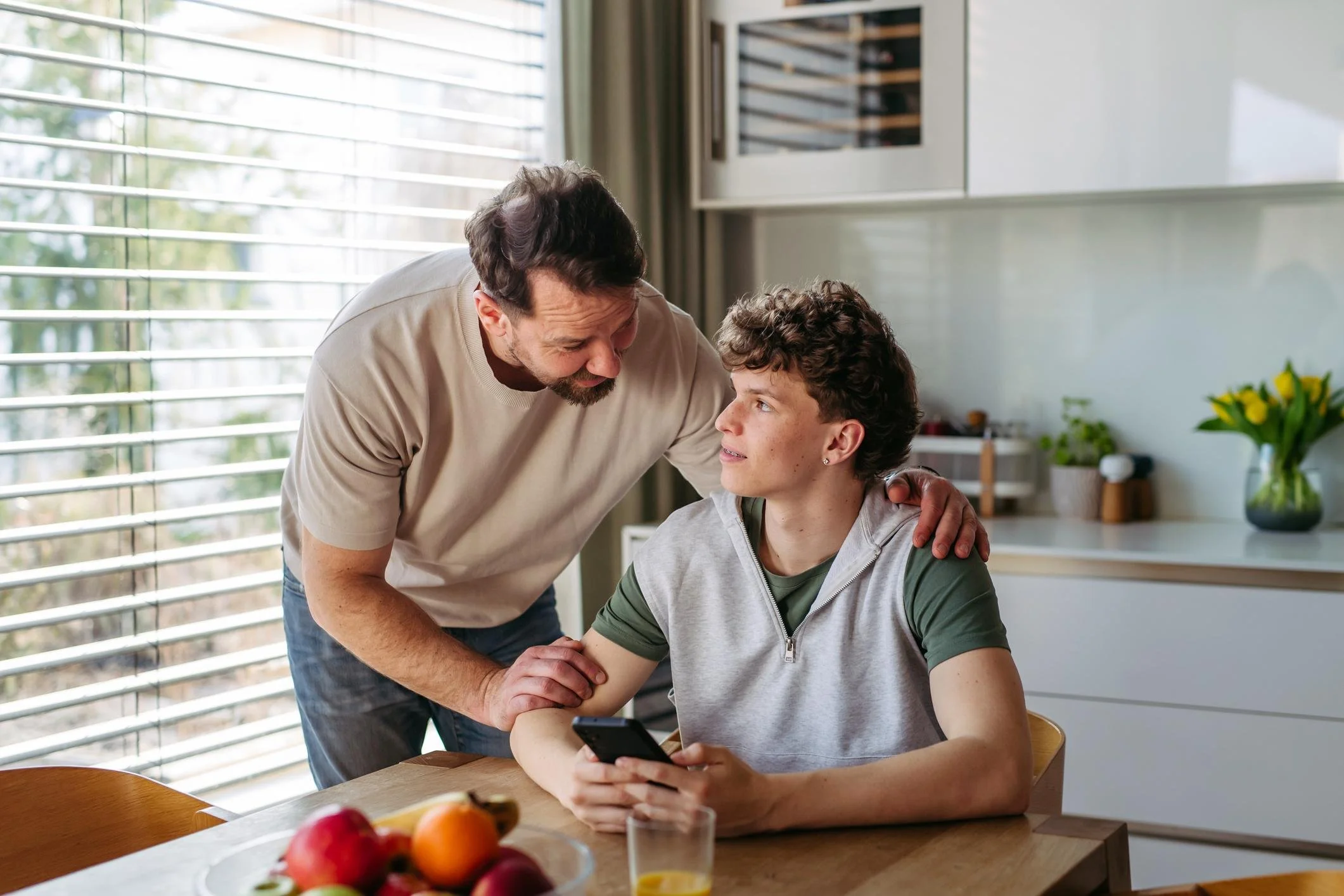 Father reassuring a teenager at a kitchen table, illustrating family support for teens with high functioning depression.