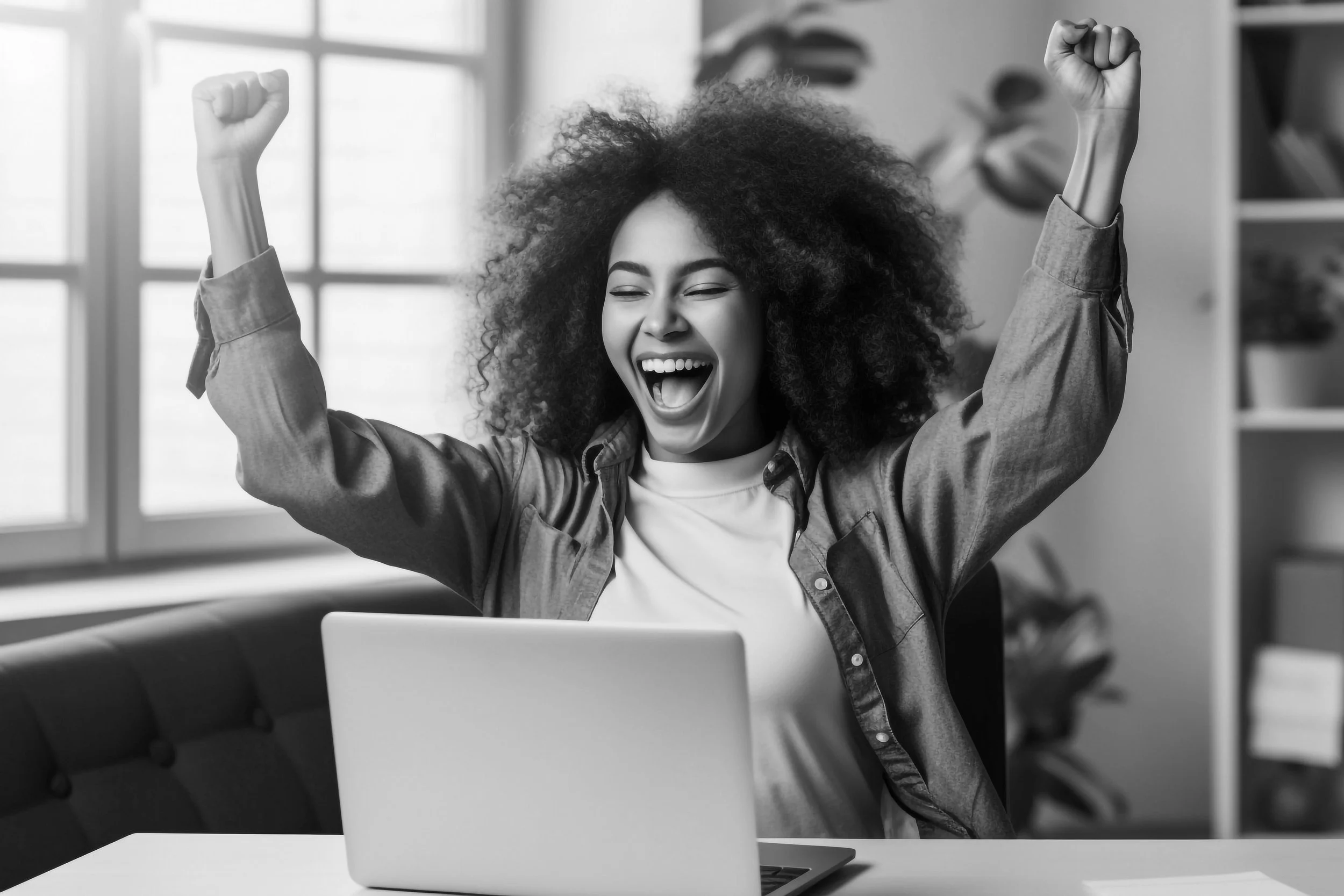 Black & white portrait of a woman business owner with hands raised over her head in celebration and smiling