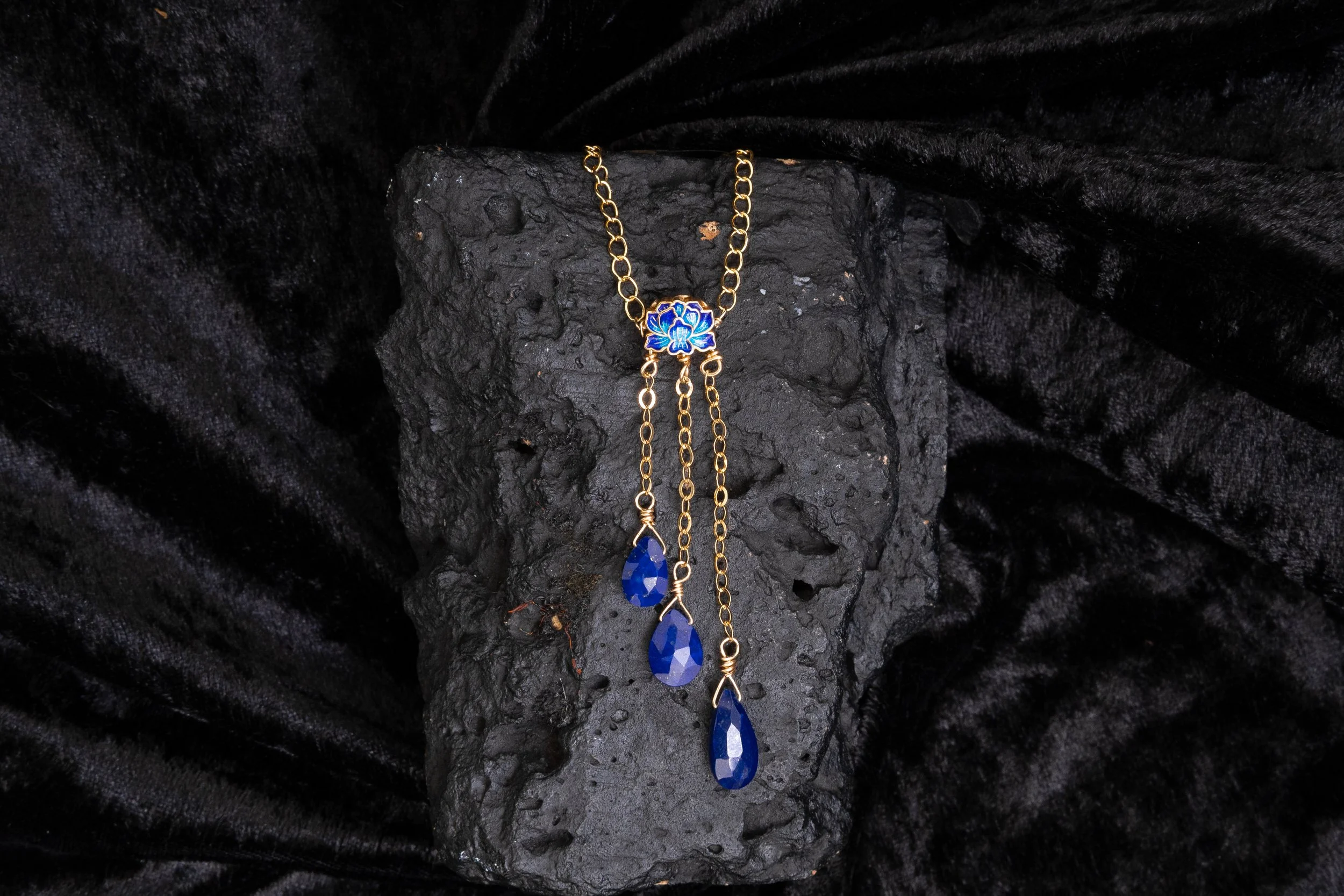 Gold chain necklaces with blue gemstones on black textured background.
