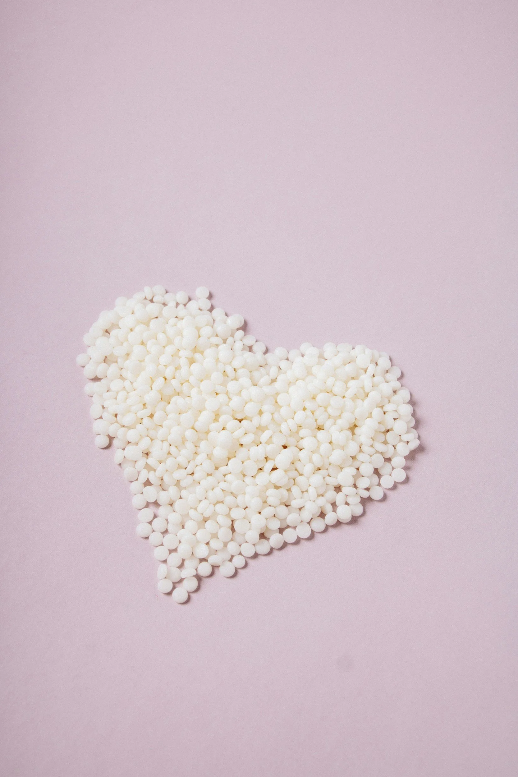 Small white spheres arranged in the shape of a heart on a pink background.