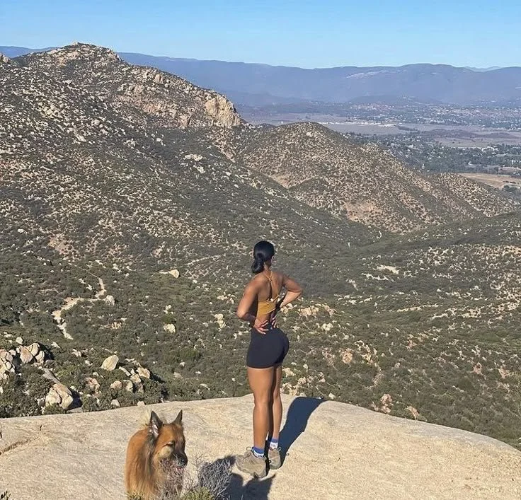 Image of woman in hiking boots with dog standing atop mountain